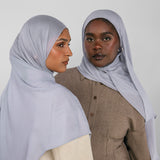 Two women wearing light blue hijabs against a white background