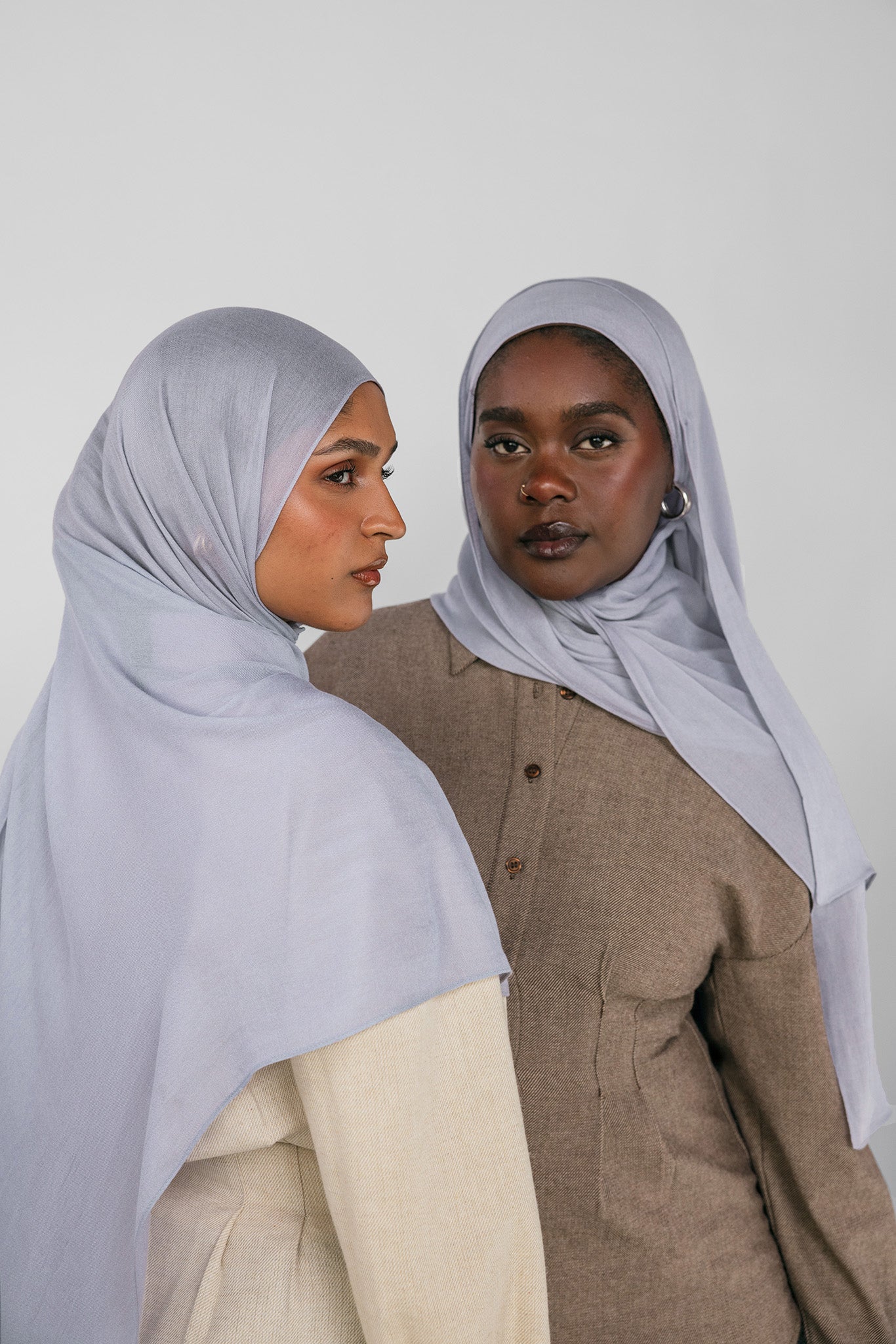 Two women wearing light blue hijabs against a white background