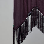A dark plum purple fabric panel with long black fringe trim along the jagged curved bottom edge, shown against a plain light gray background.