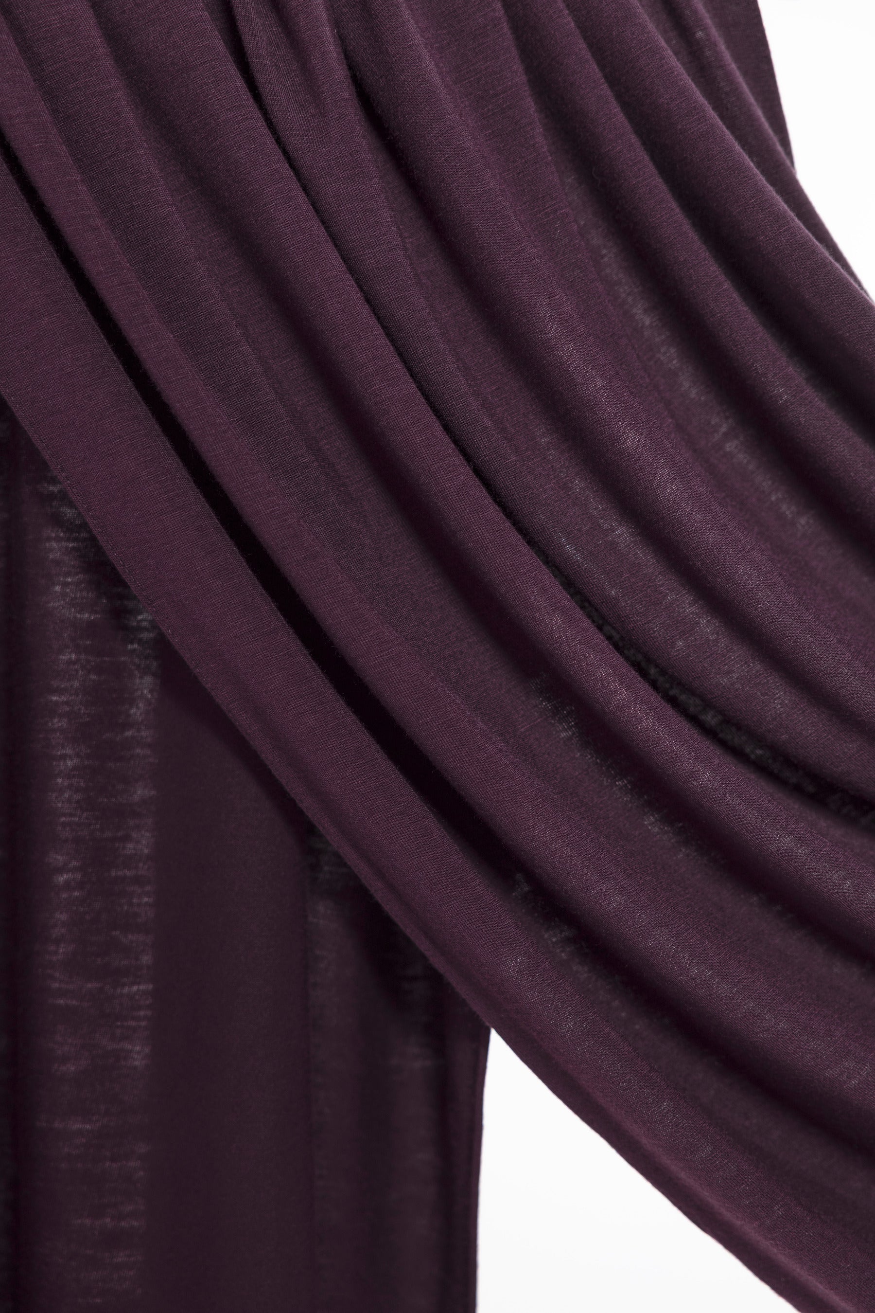 A close-up of draped dark plum purple fabric with a subtle sheen, showing the texture and folds against a white background.