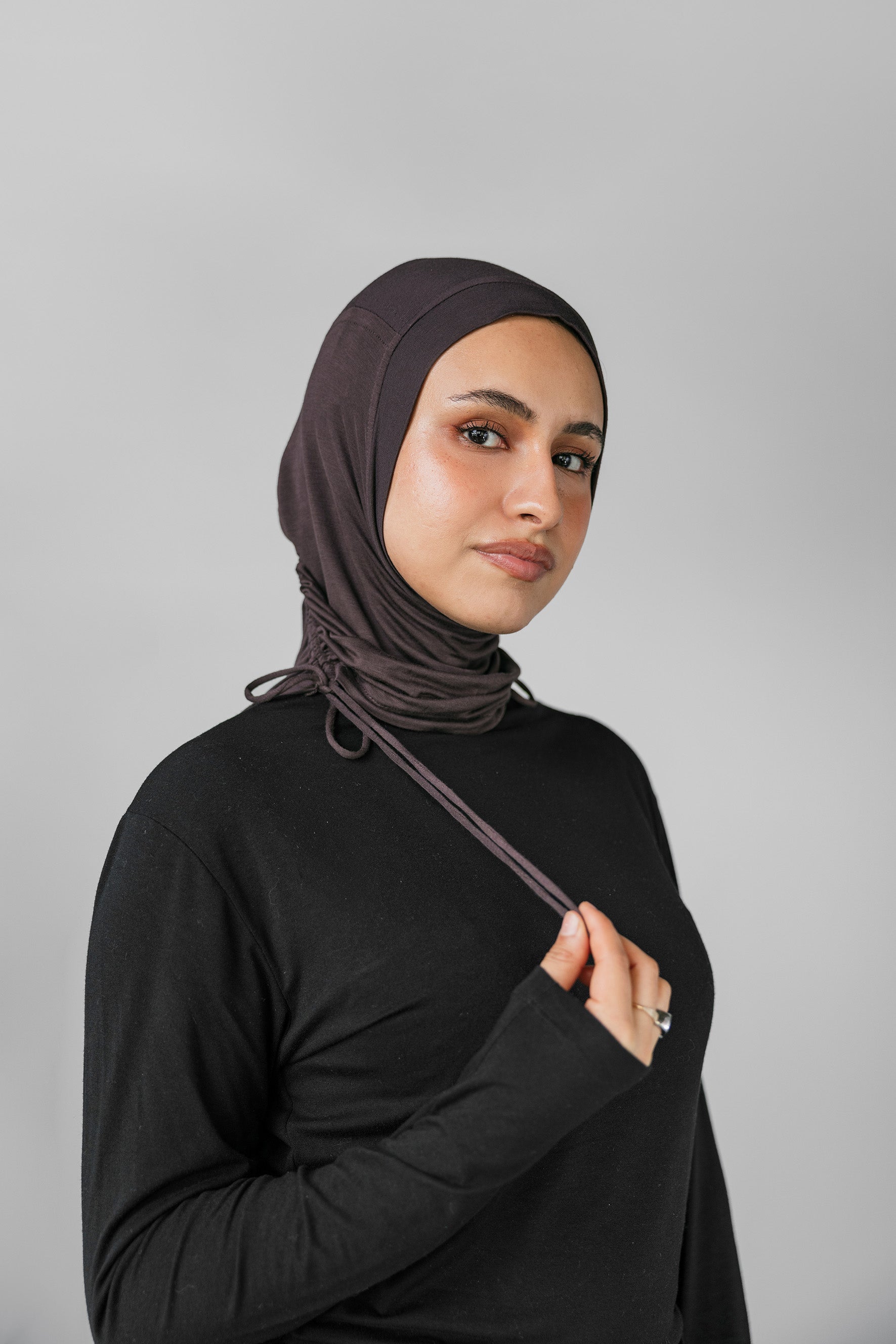 Woman wearing a black hijab against a gray background