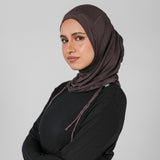 Woman wearing a brown hijab and black outfit against a gray background