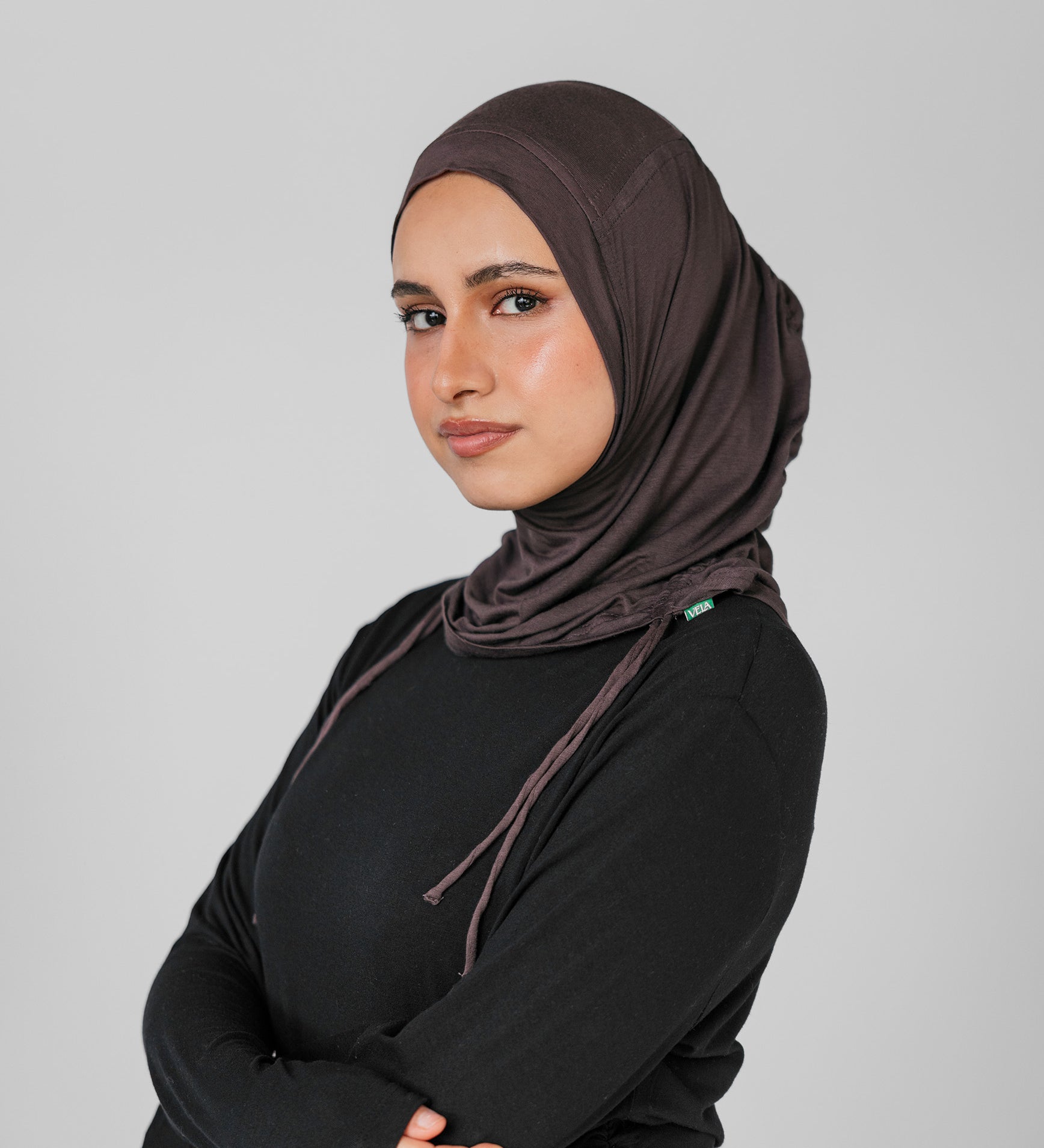 Woman wearing a brown hijab and black outfit against a gray background