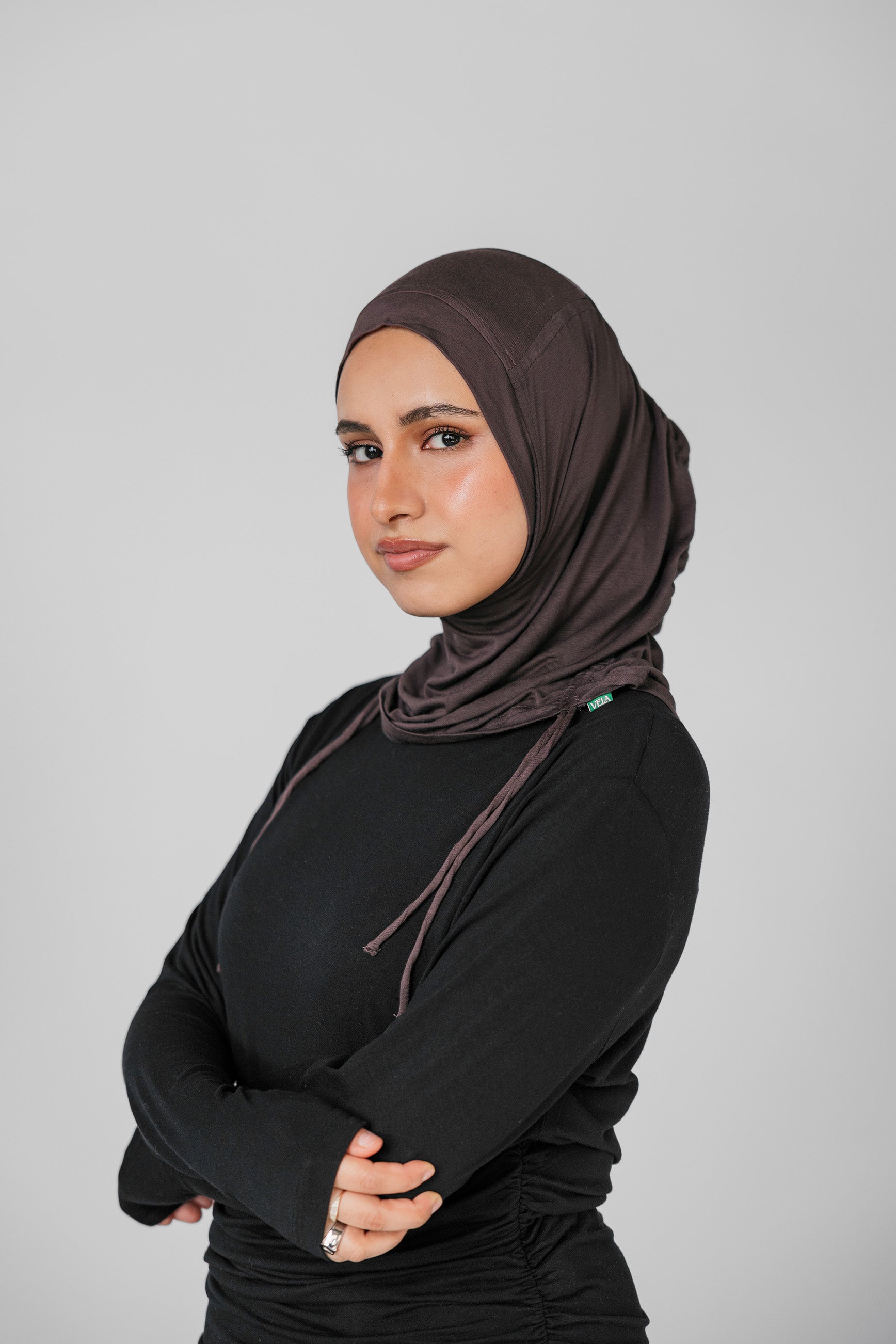 Woman wearing a brown hijab and black outfit against a gray background