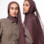 Two women modeling matching plum-colored hijabs and coordinated taupe button-front tops against a plain light gray studio background.