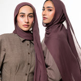 Two women modeling matching plum-colored hijabs and coordinated taupe button-front tops against a plain light gray studio background.