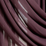 A close-up of draped sheer curtains in a deep plum purple color, showing the fabric's soft texture and light filtering through the folds.