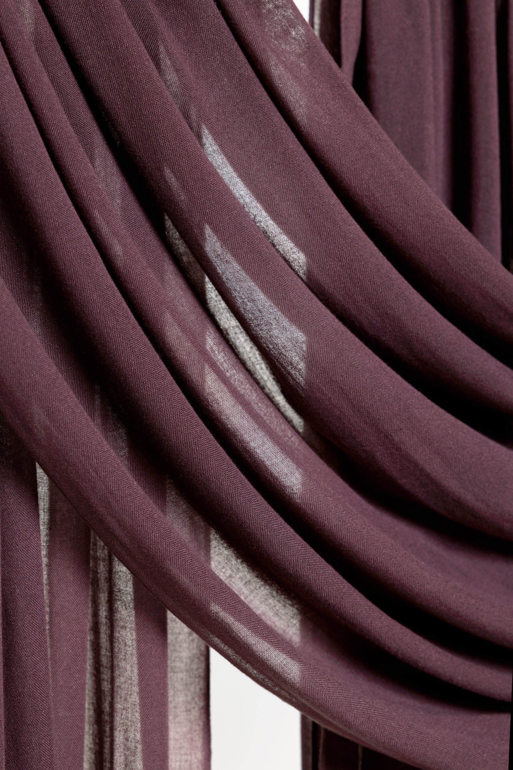 A close-up of draped sheer curtains in a deep plum purple color, showing the fabric's soft texture and light filtering through the folds.