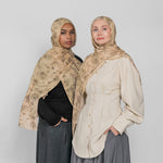 Two women wearing hijabs and long skirts against a plain background