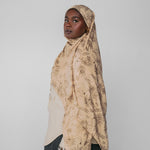 Woman wearing a beige patterned hijab against a plain background