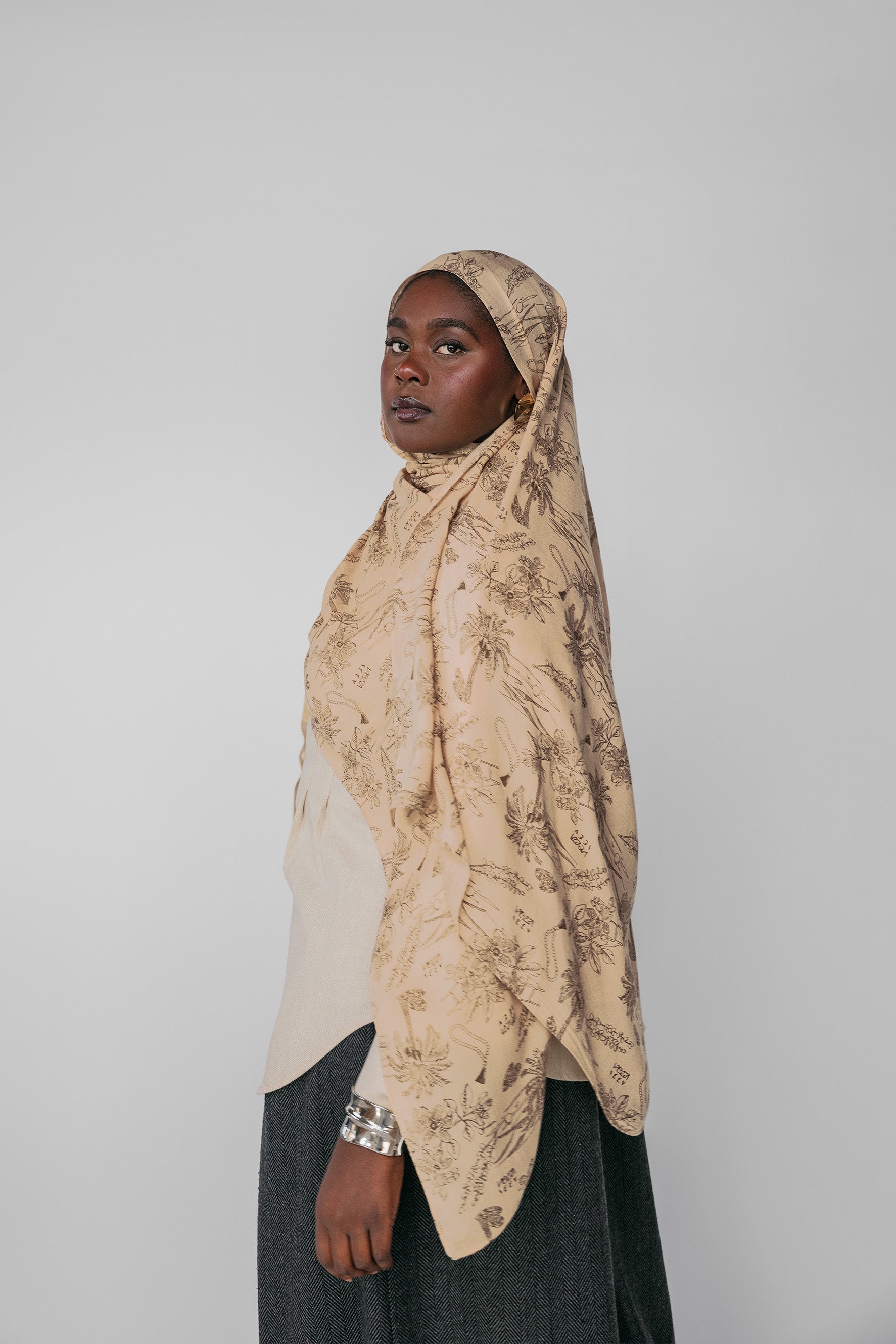 Woman wearing a beige patterned hijab against a plain background