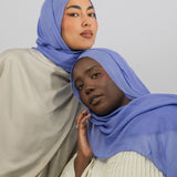 Two women wearing blue hijabs against a plain background