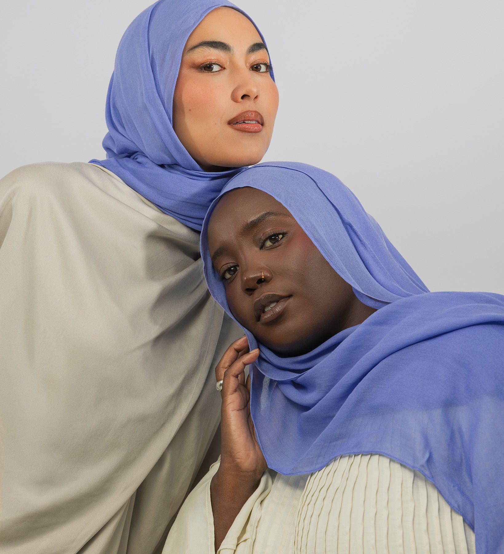 Two women wearing blue hijabs against a plain background