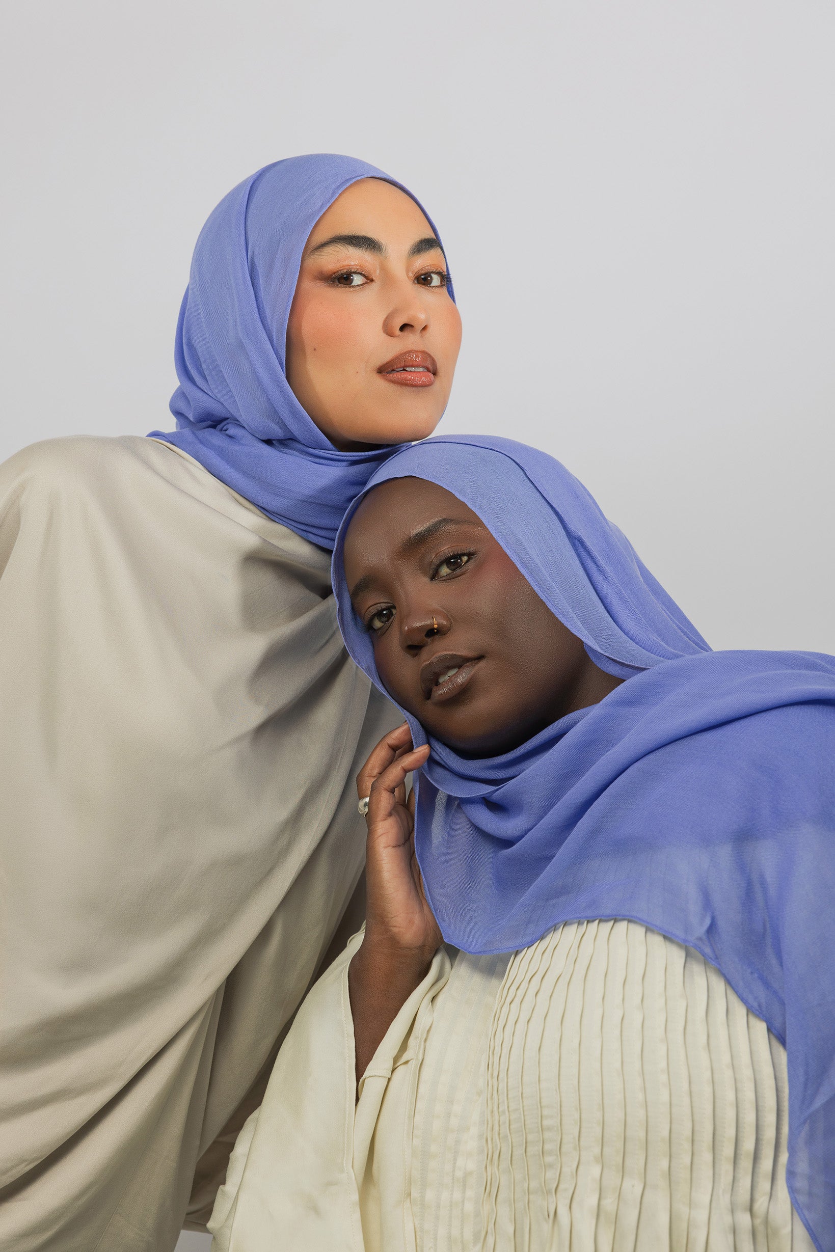Two women wearing blue hijabs against a plain background