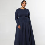 A woman modeling a long-sleeve navy blue maxi dress with a fitted bodice and a full, flowing skirt, standing against a plain light gray studio background.