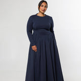 A woman modeling a long-sleeve navy blue maxi dress with a fitted bodice and a full, flowing skirt, standing against a plain light gray studio background.
