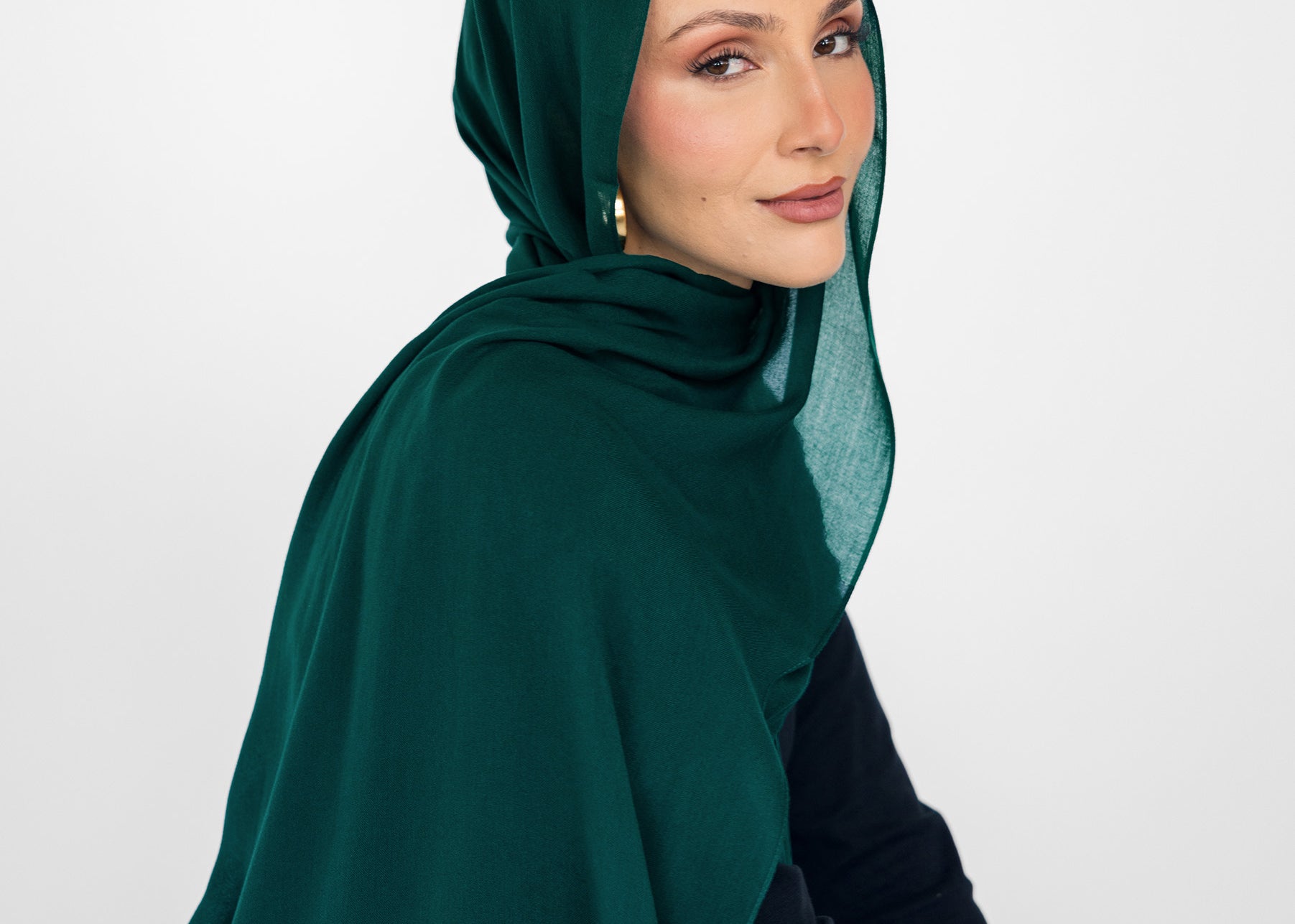 Woman wearing a green hijab and black outfit against a white background