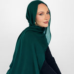 Woman wearing a green hijab and black outfit against a white background