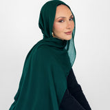 Woman wearing a green hijab and black outfit against a white background