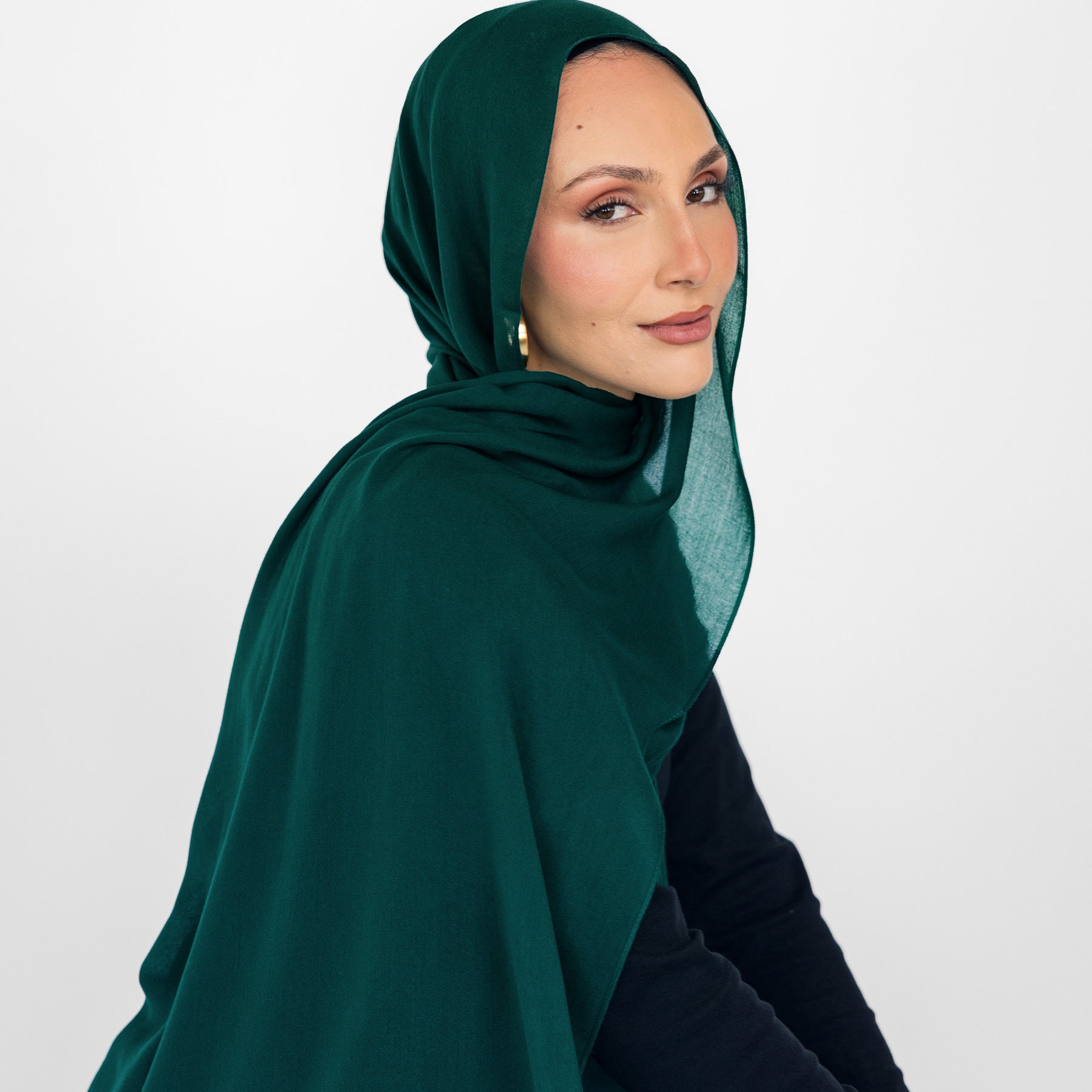 Woman wearing a green hijab and black outfit against a white background