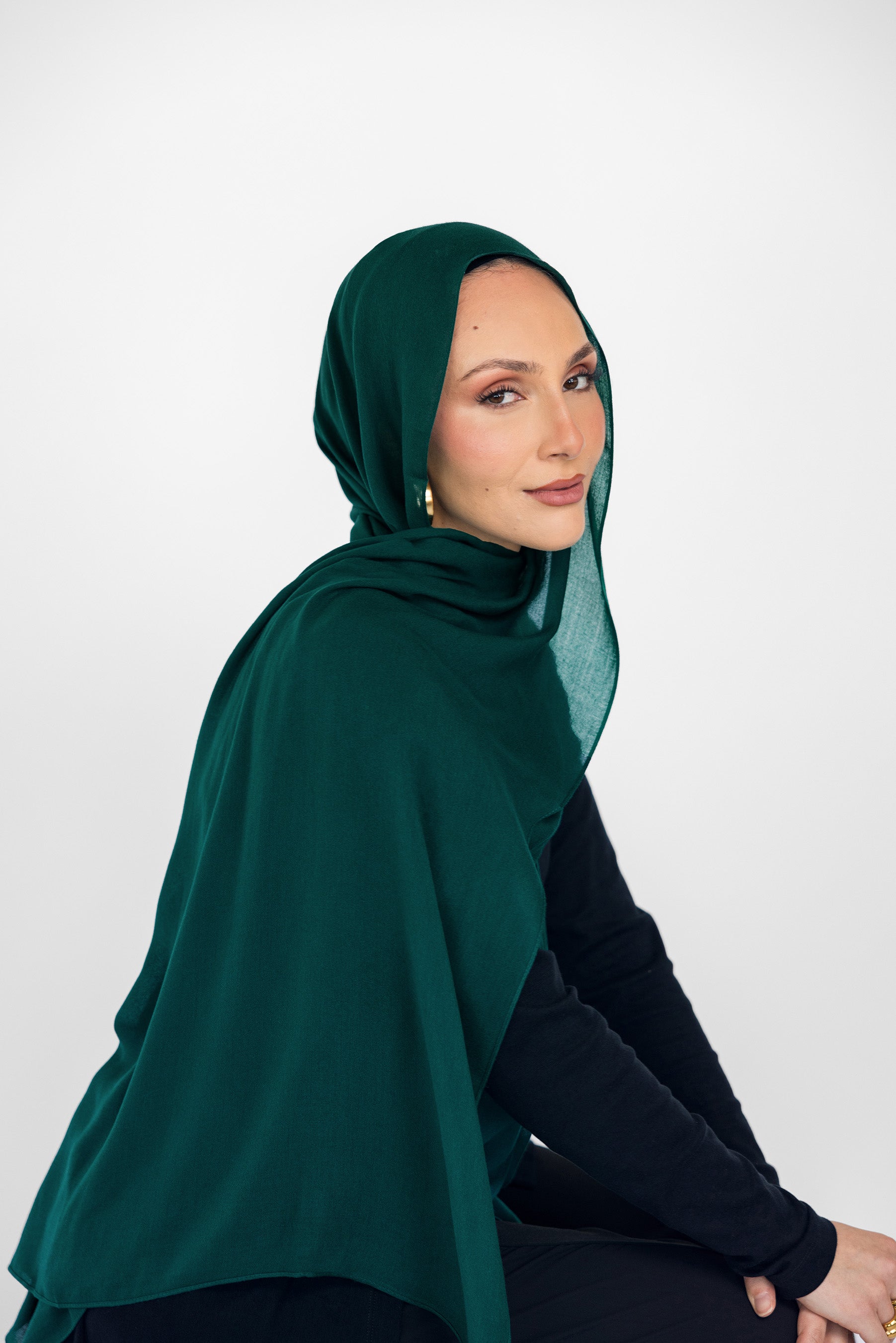 Woman wearing a green hijab and black outfit against a white background