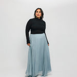 Woman wearing a black top and light blue skirt on a white background