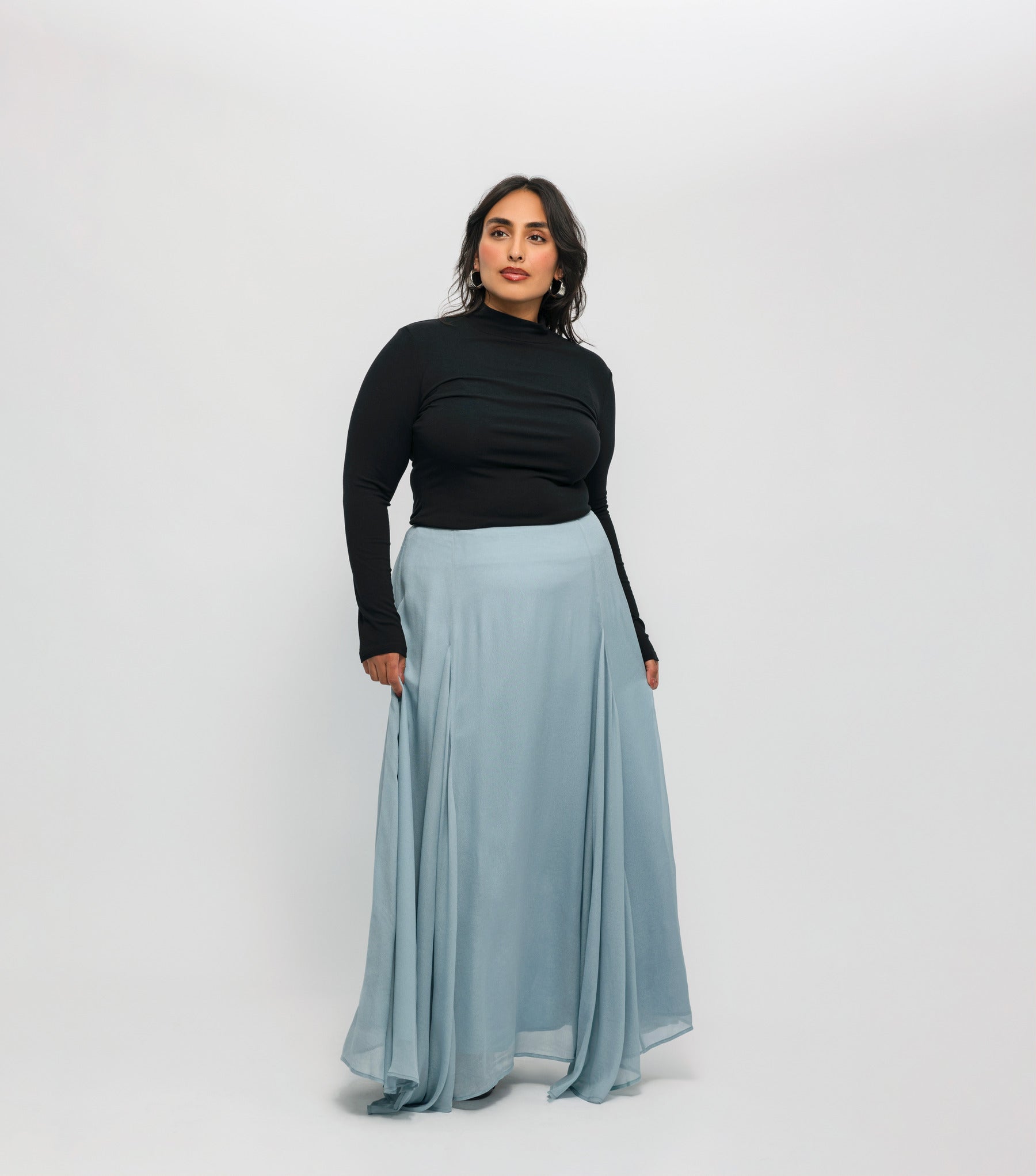 Woman wearing a black top and light blue skirt on a white background