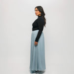 Woman wearing a black top and light blue skirt against a white background