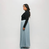 Woman wearing a black top and light blue skirt against a white background