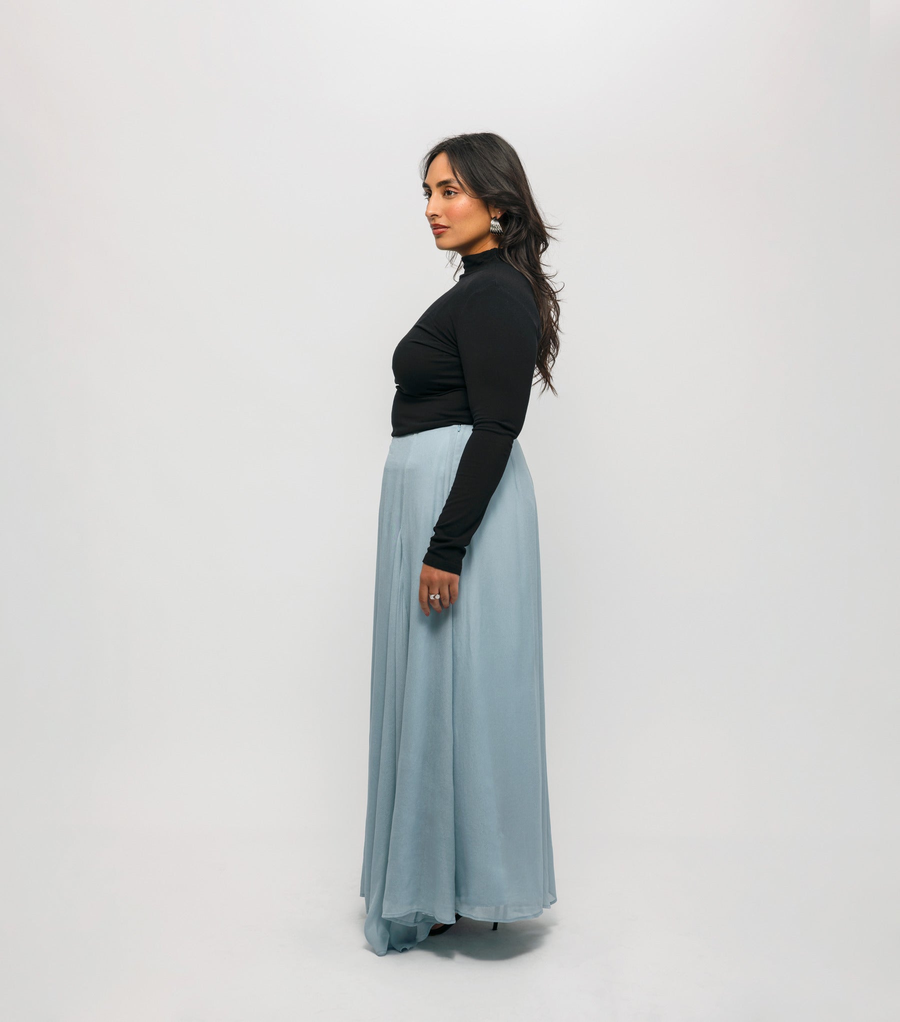 Woman wearing a black top and light blue skirt against a white background