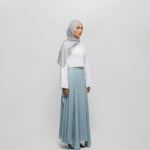 Woman wearing a light gray hijab, white top, and light blue skirt on a white background