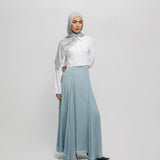 Woman wearing a hijab, white blouse, and light blue skirt on a plain background