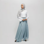 Woman wearing a light gray hijab, white top, and light blue skirt on a white background