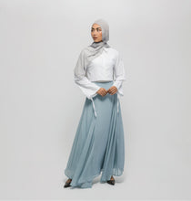 Woman wearing a light gray hijab, white top, and light blue skirt on a white background
