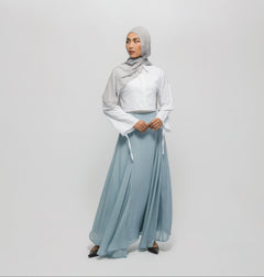 Woman wearing a light gray hijab, white top, and light blue skirt on a white background