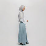 Woman wearing a light gray hijab and light blue skirt on a white background