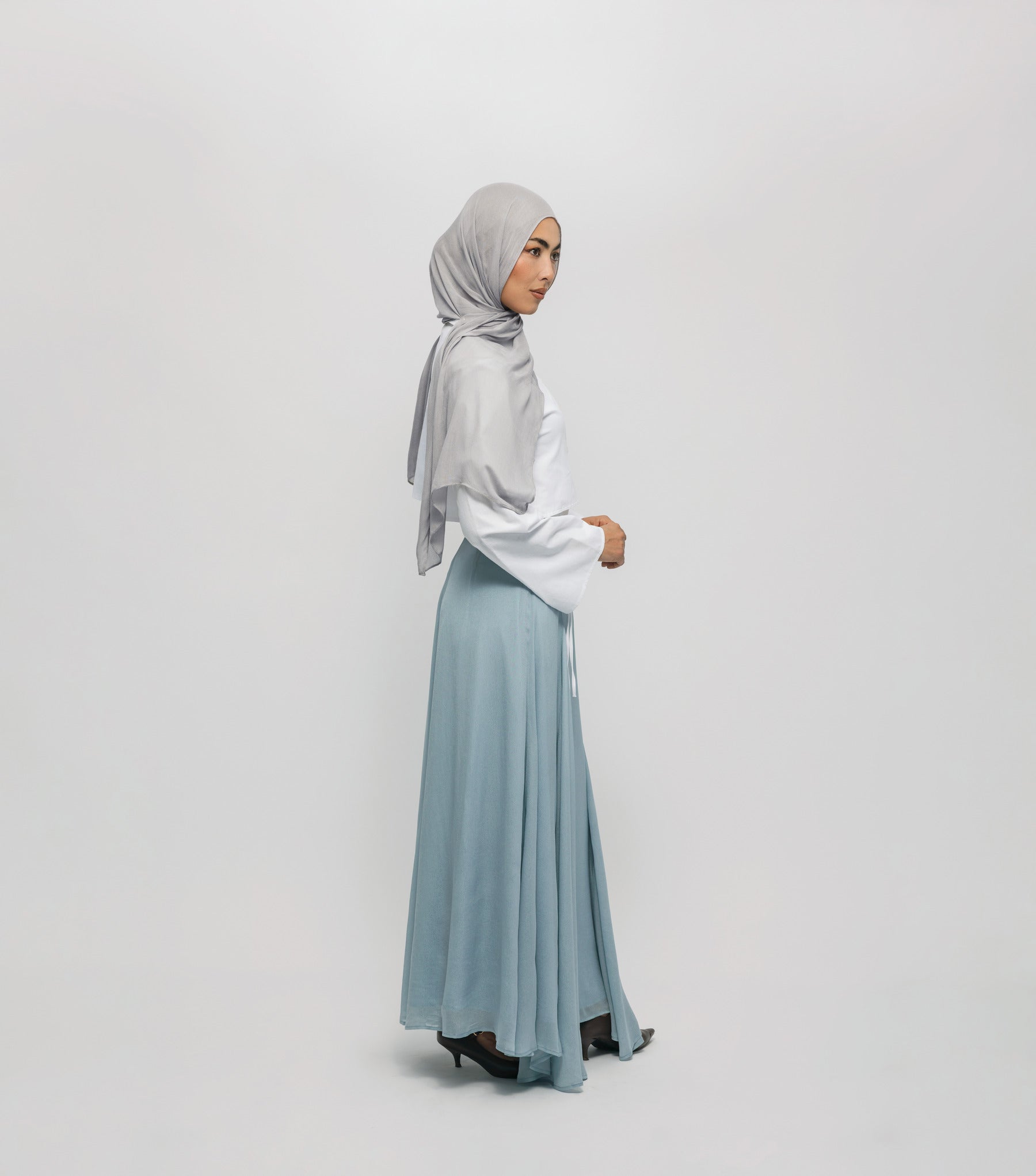 Woman wearing a light gray hijab and light blue skirt on a white background