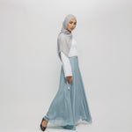 Woman wearing a gray hijab and light blue skirt on a white background