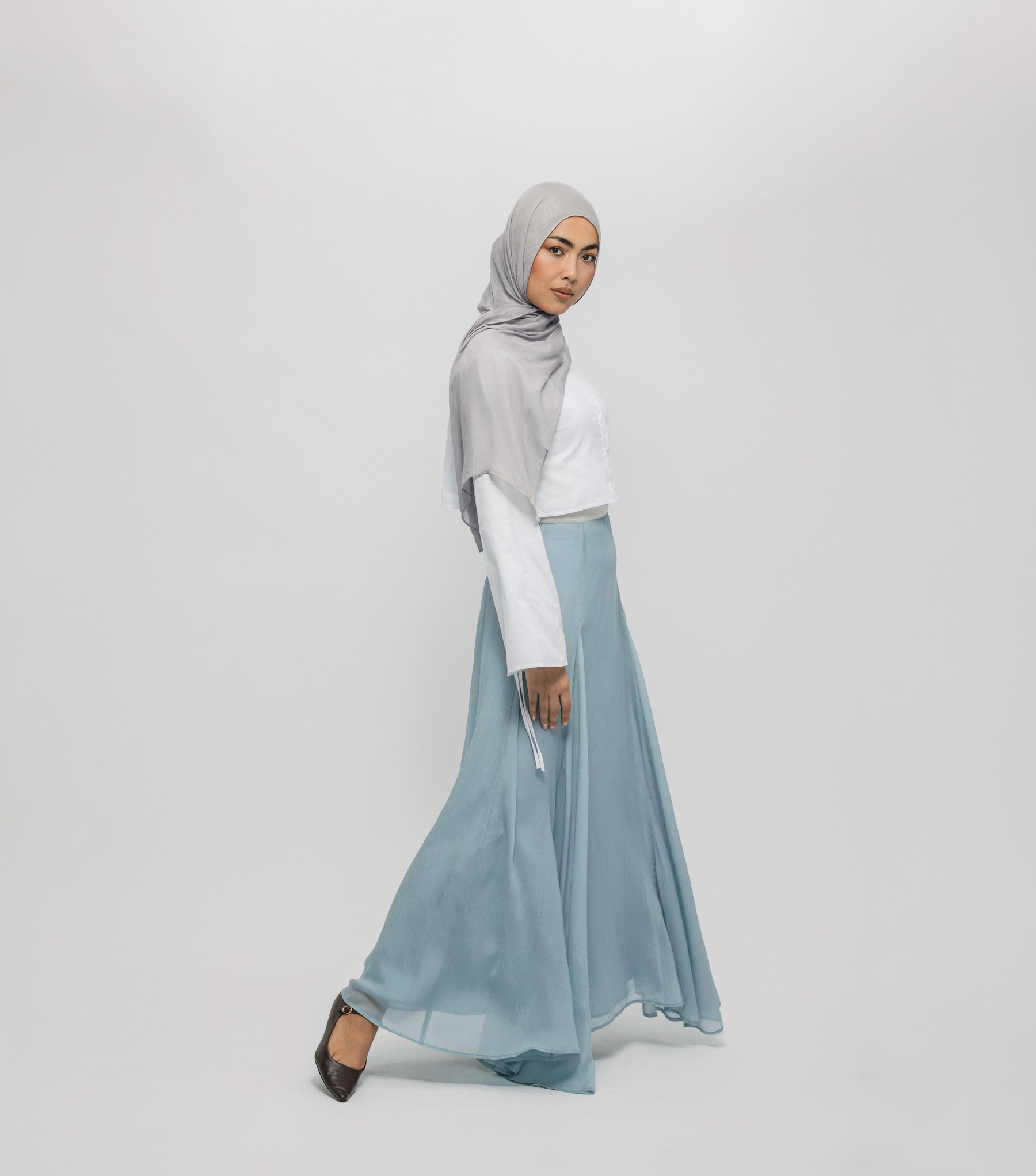 Woman wearing a gray hijab and light blue skirt on a white background