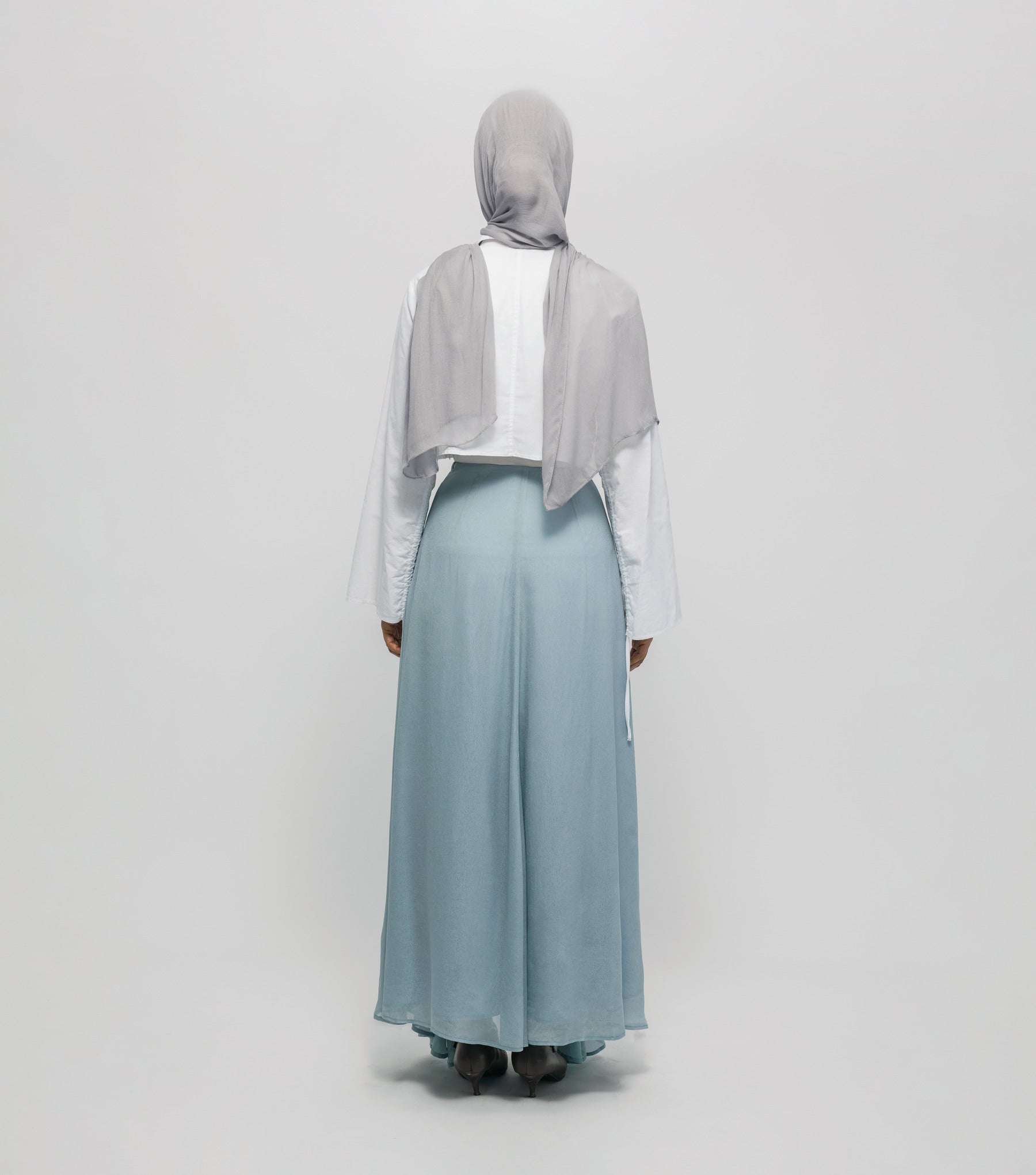 Person wearing a light gray hijab, white top, and light blue skirt on a white background