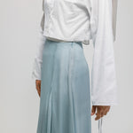 Person wearing a white shirt and light blue skirt on a plain background