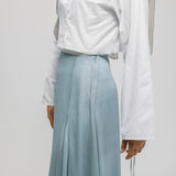Person wearing a white shirt and light blue skirt on a plain background