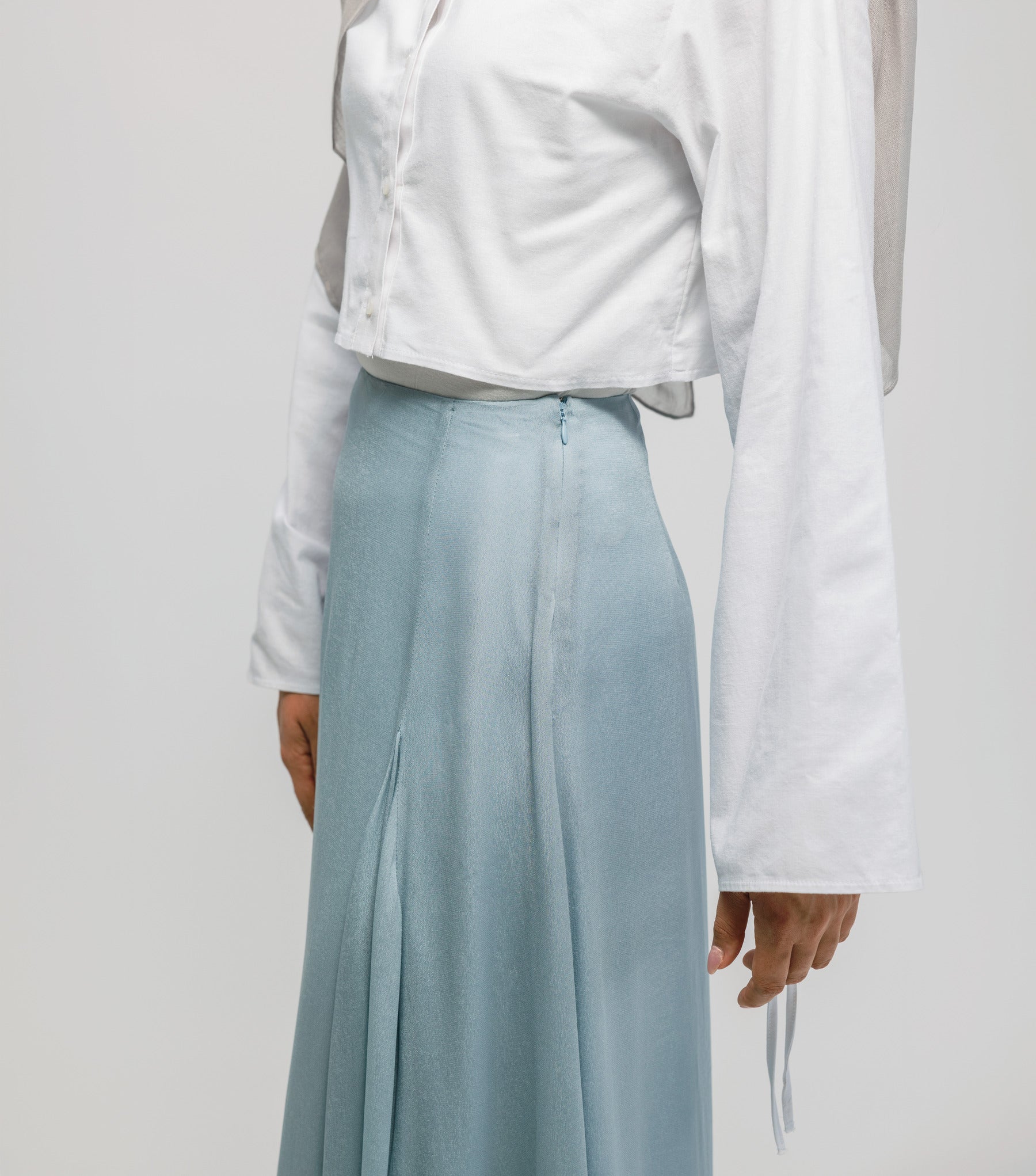 Person wearing a white shirt and light blue skirt on a plain background