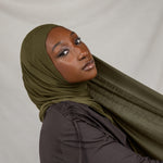 Woman wearing a green hijab and dark clothing against a white background