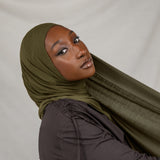 Woman wearing a green hijab and dark clothing against a white background