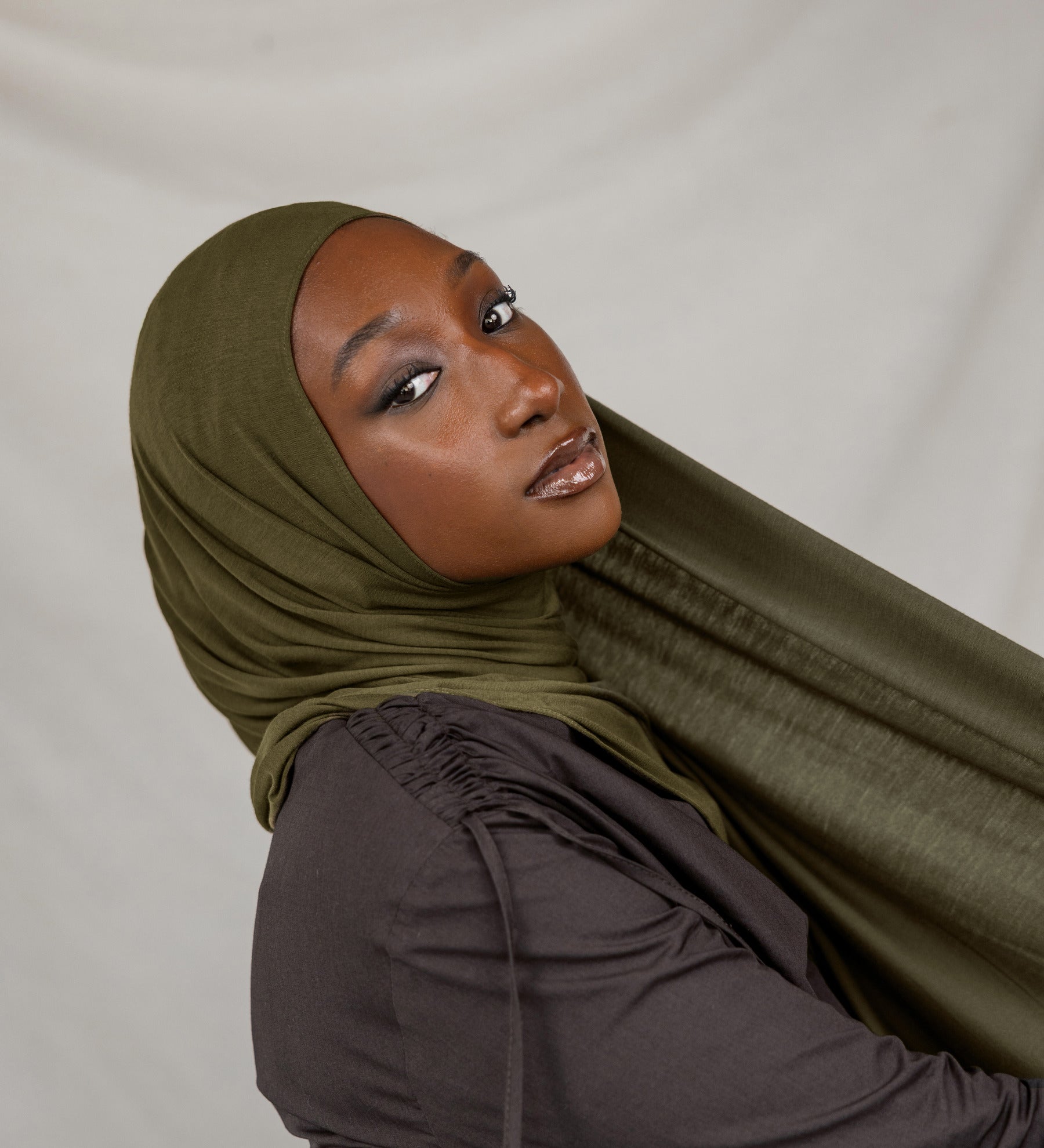 Woman wearing a green hijab and dark clothing against a white background