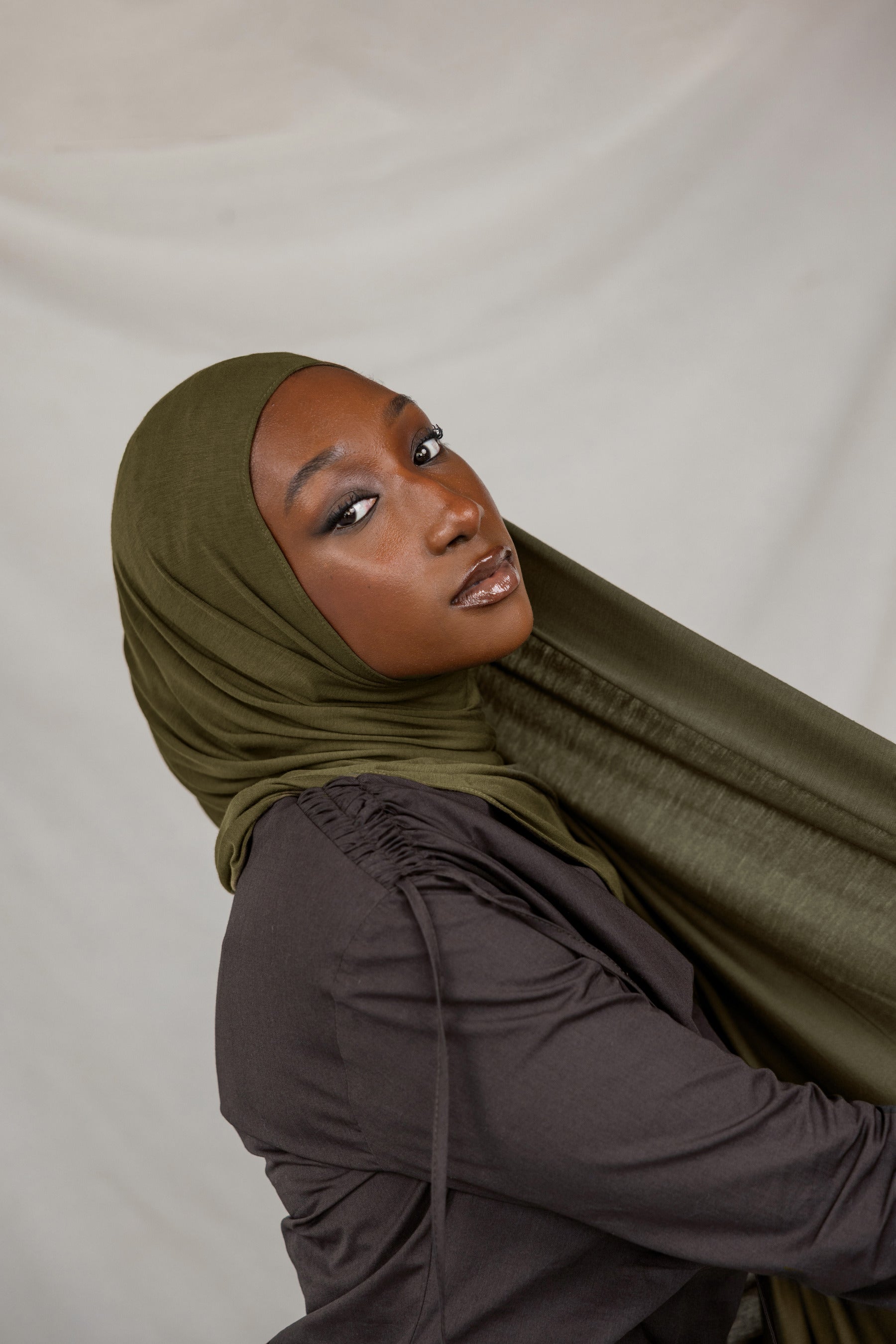 Woman wearing a green hijab and dark clothing against a white background