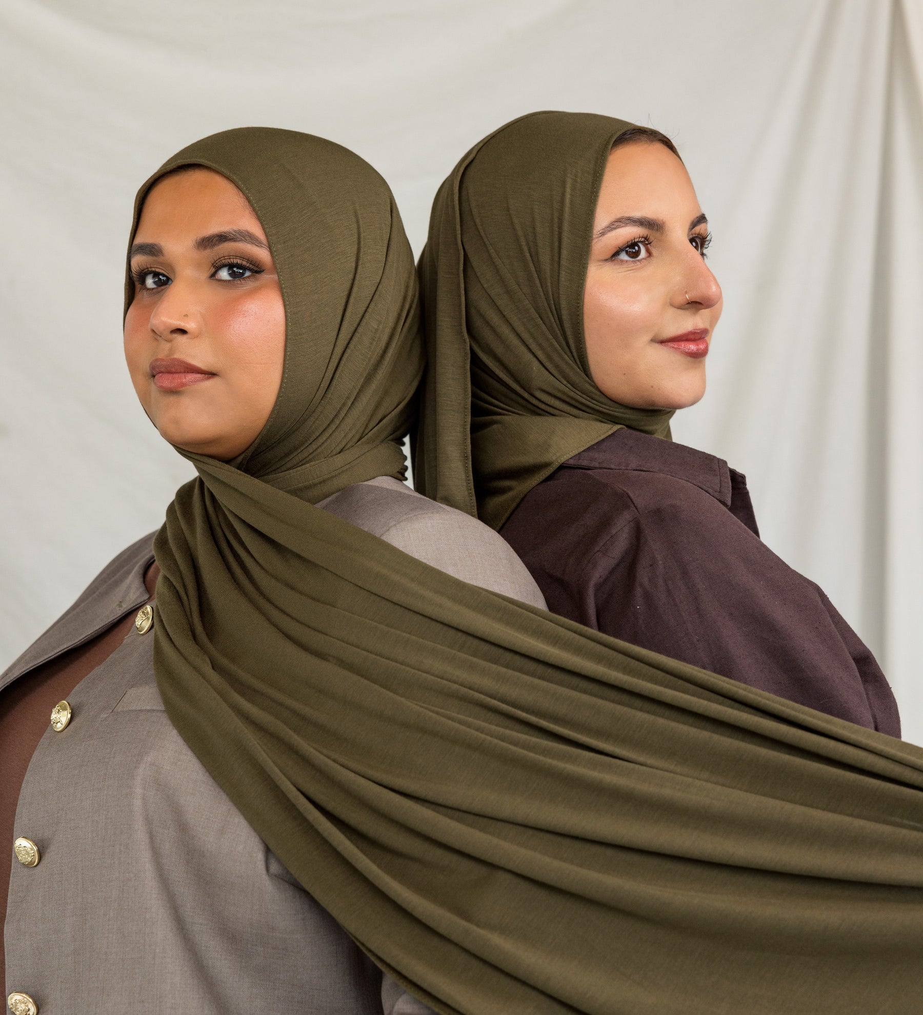 Woman wearing a green hijab and dark clothing against a white background