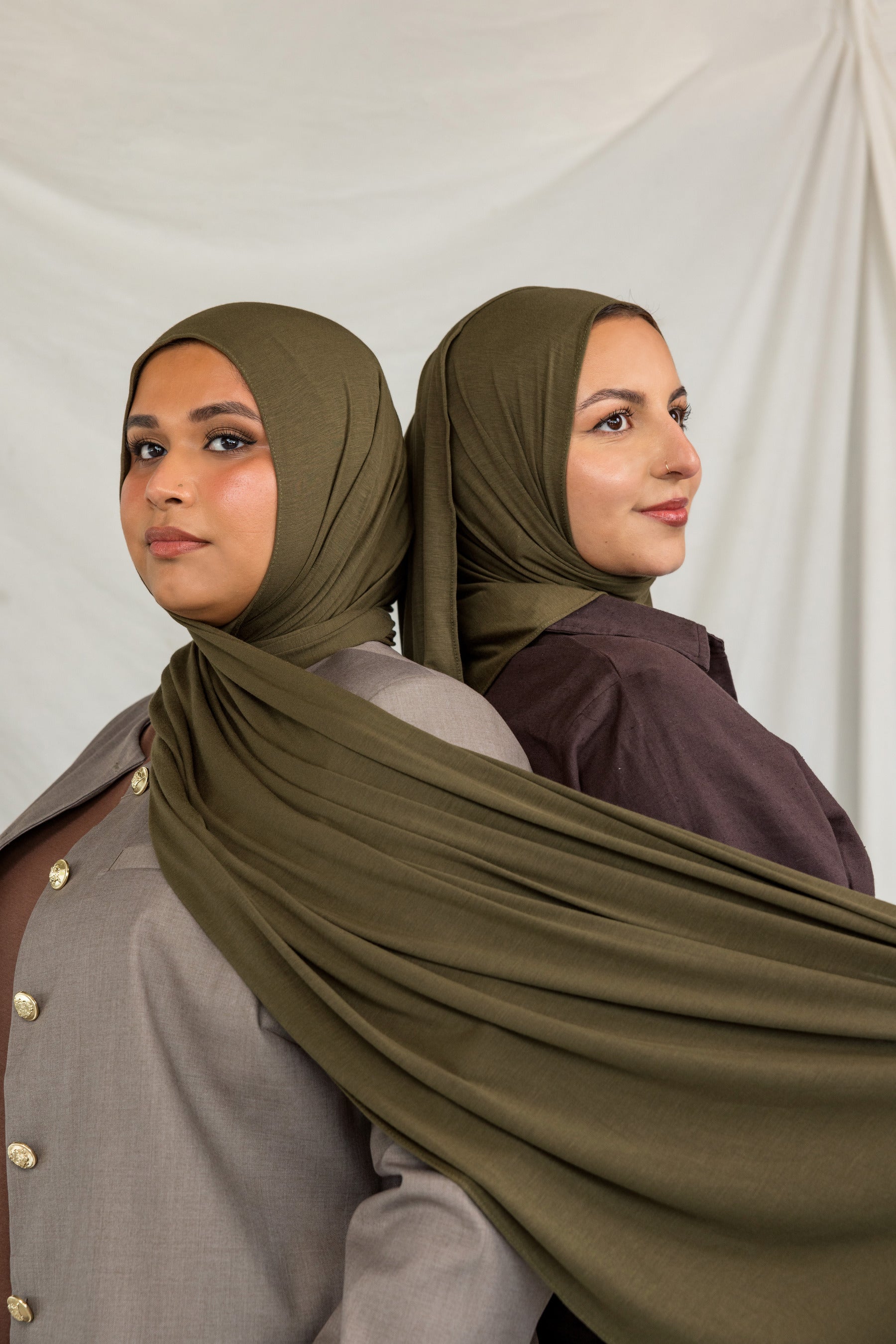 Woman wearing a green hijab and dark clothing against a white background