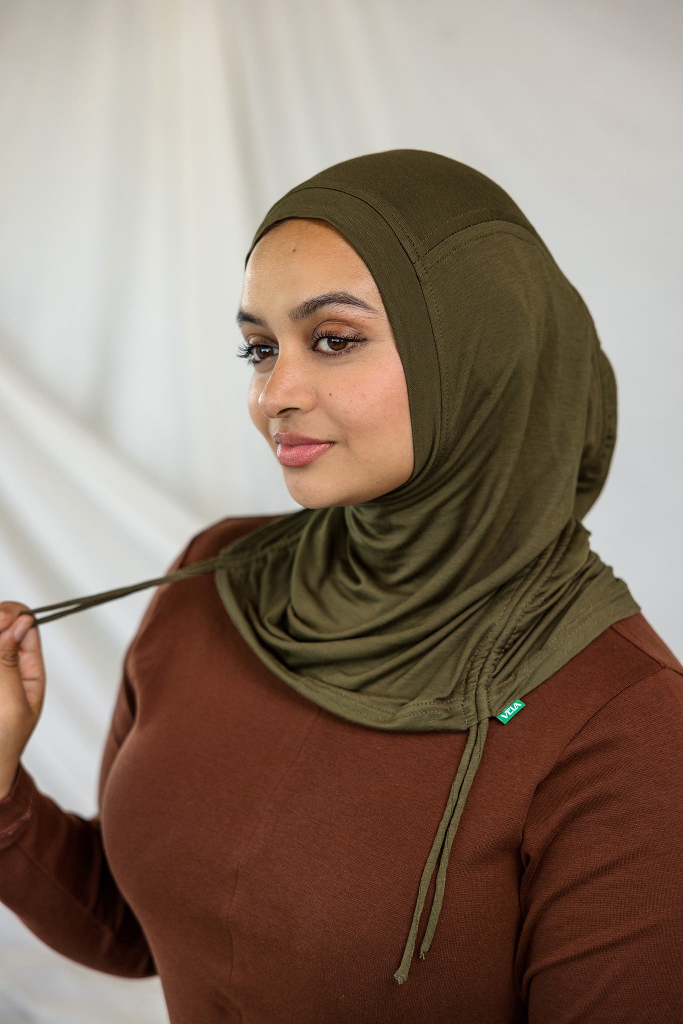 Woman wearing an olive green hijab against a white background